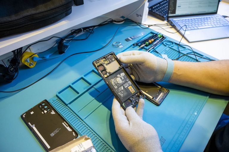 Un technicien répare un smartphone dans une entreprise spécialisée.
