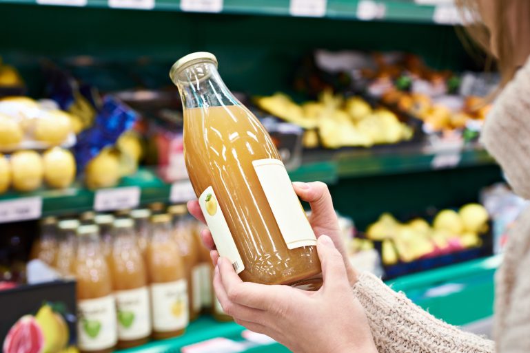 une consommatrice lit l’étiquette d’un jus de pomme