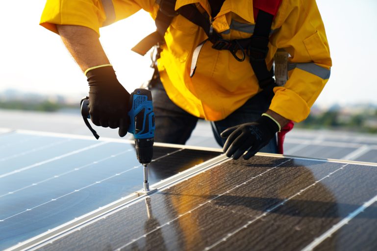 Un installateur visse un panneau solaire sur un toit