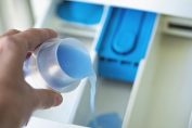 Un homme verse de la lessive liquide dans le bac de sa machine à laver.