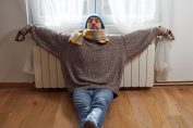 un homme collé au radiateur avec un bonnet, une écharpe et un pull