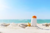 Un flacon de crème solaire planté dans le sable d'une plage
