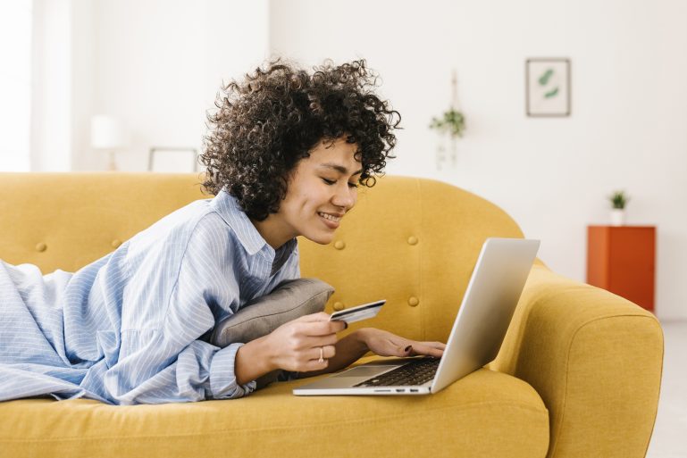 une jeune femme devant son ordinateur, carte bancaire à la main