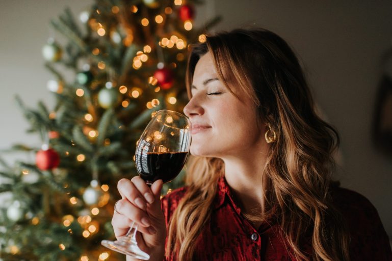 Une jeune femme buvant un verre de vin devant un sapin de noël.