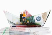 Deux figurines de retraités assis sur un voilier en billets d'euros pliés.