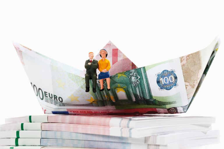Deux figurines de retraités assis sur un voilier en billets d'euros pliés.