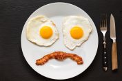 Des œufs frits à la poêle et un morceaux de bacon figurant un visage triste