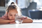 Une petite fille regarde un verre d'eau posé sur une table