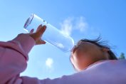 Une petite fille boit à la gourde de l'eau du robinet