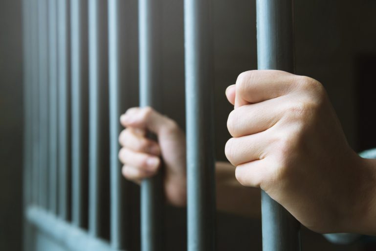 des mains agrippant des barreaux de prison