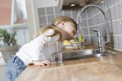Une petite fille bois de l'eau au robinet