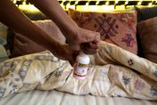 Un homme en train d'ouvrir un flacon de Sniper 100 sur un lit