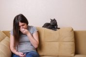 Une jeune femme éternue à côté de son chat
