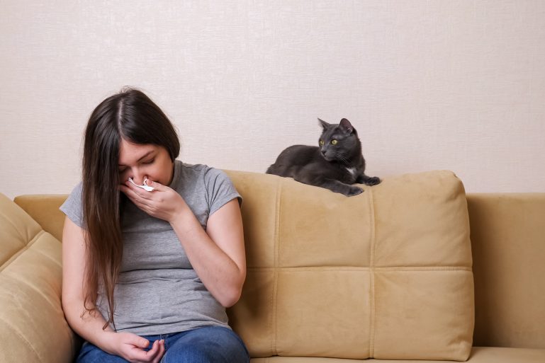 Une jeune femme éternue à côté de son chat