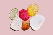 Plusieurs crèmes exfoliantes colorées étalées sur un fond rose
