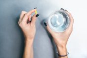 Mains de femme tenant une gélule et un verre d'eau