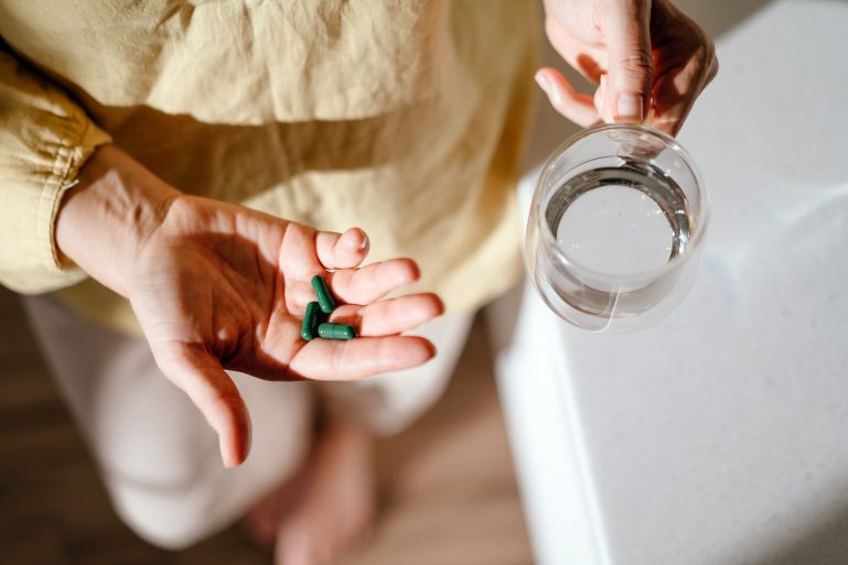 Femme tenant dans ses mains des gélules et un verre d’eau