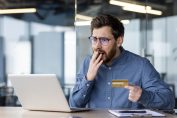 Un homme tenant une carte de crédit à la main a l’air choqué par l’écran