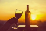 Une main féminine avec un verre de vin et une bouteille sur un fond de coucher de soleil