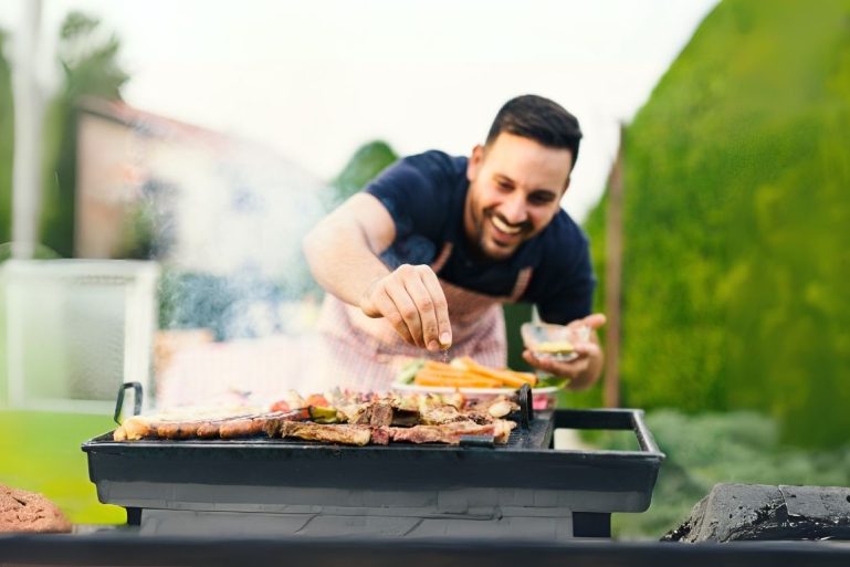 Un homme mets des épices sur de la viande qui cuit sur un barbecue
