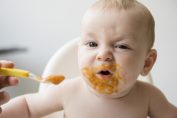 Un bébé grimace en mangeant un petit pot