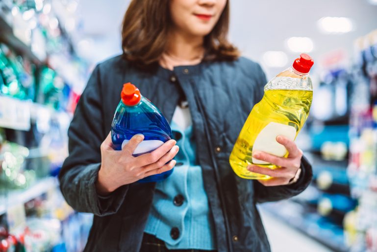 Une femme hésite entre deux produits nettoyants en agasins