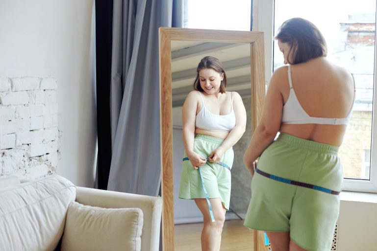 Une jeune femme mesure sa taille en souriant