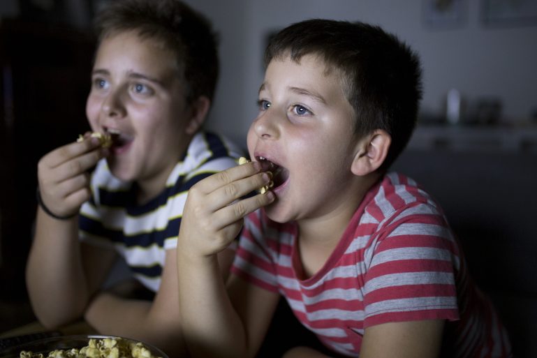 Deux garçons mangent devant la télévision