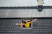 Une femme sort d'un velux sur un toit équipé de panneaux solaires