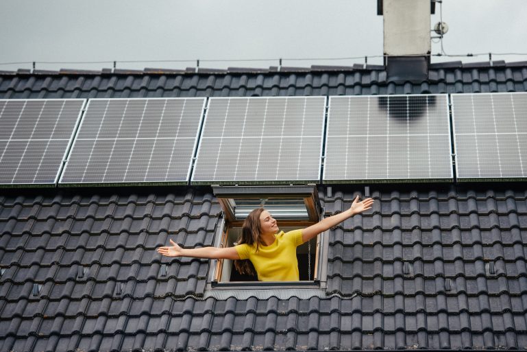 Une femme sort d'un velux sur un toit équipé de panneaux solaires