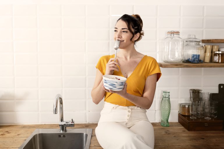 Une jeune femme mange dans sa cuisine