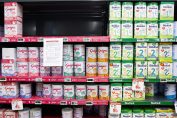 Une avis de rappel de produit est attaché à une étagère de lait infantile dans un rayon de supermarché.