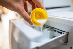 Une personne verse un bouchon de lessive liquide dans une machine à laver