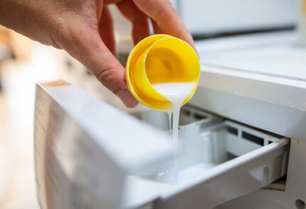 Une personne verse un bouchon de lessive liquide dans une machine à laver